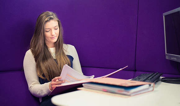 A ֱ student reading over their work against a purple wall