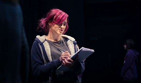A ֱ stage management student reading and making notes on a notepad on stage
