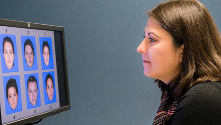 ֱ Psychology Student looking at a computer screen displaying 6 different faces numbered 1-6