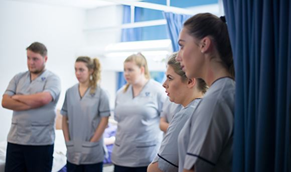 A row of ֱ student nurses listening intently as a senior nurse speaks to them