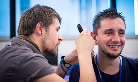ֱ Hearing Aid Audiology student using a piece of equipment to test another student's hearing