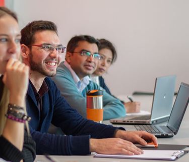 ֱ International Management with Leadership students sitting in class smiling with laptops or pads of paper and pens infront of them